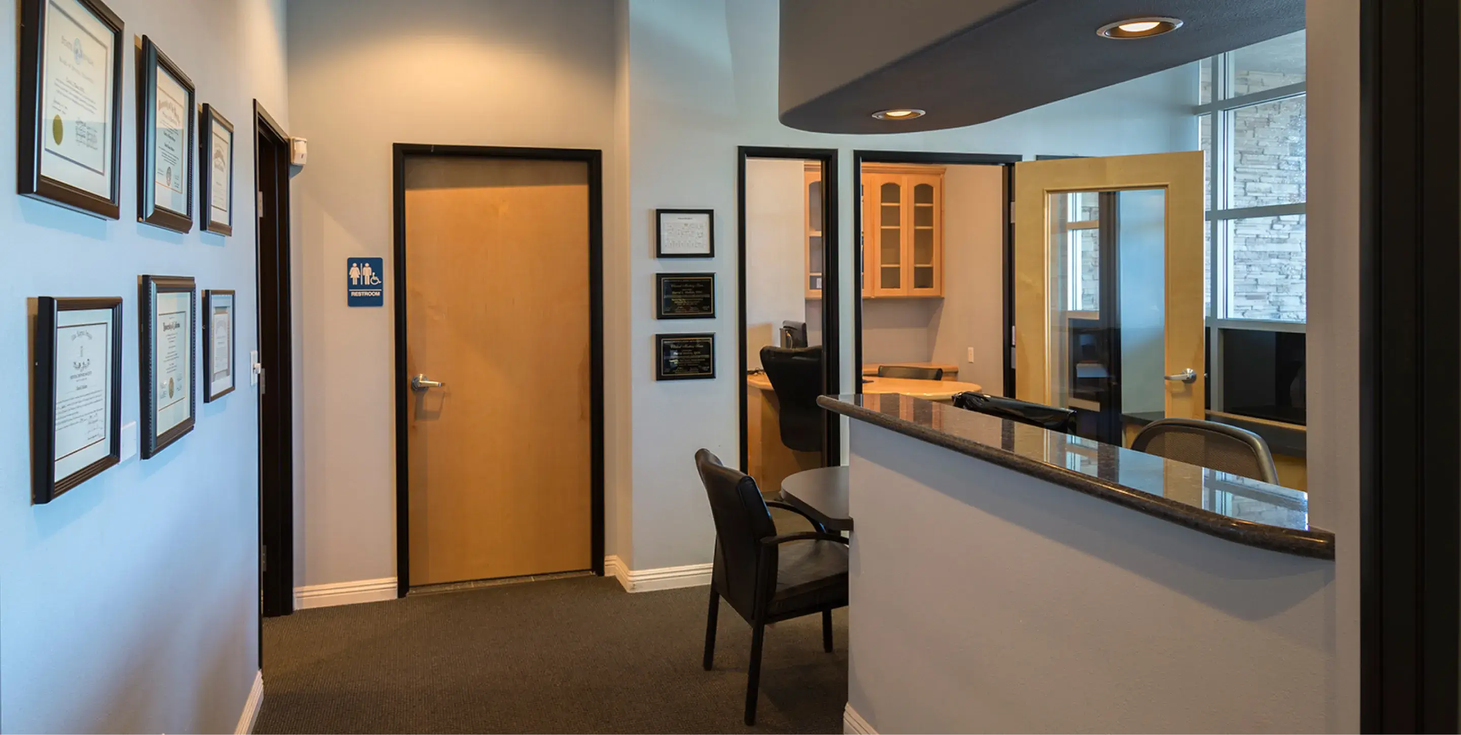 Office reception area with an empty desk, chairs, and framed certificates on the wall.