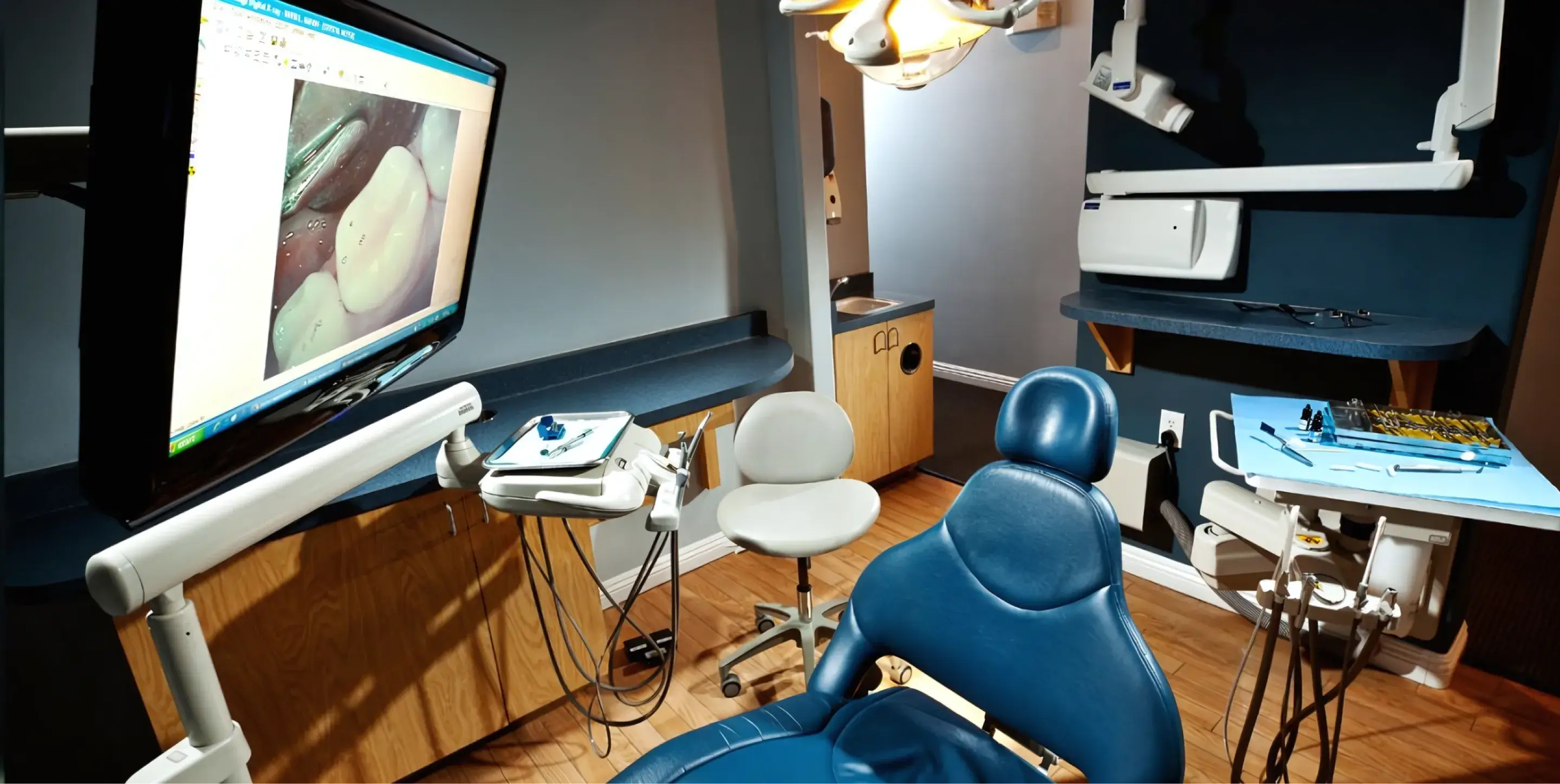 Dental examination room with a patient chair, monitor showing a tooth, and dental equipment.